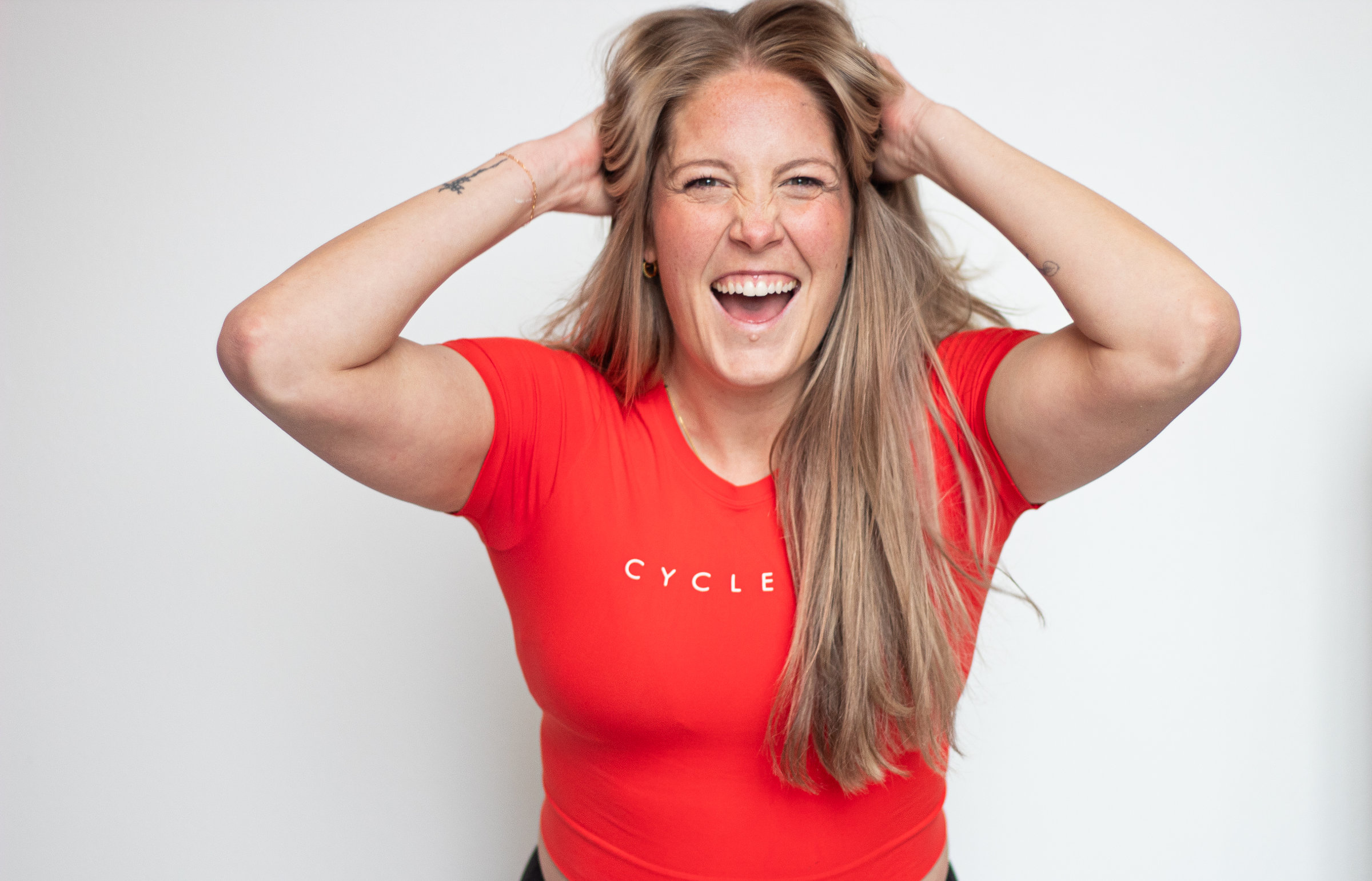 Sarah Shipp wearing a bright red t-shirt with the word 'CYCLE' smiling broadly with her hands raised to her head.